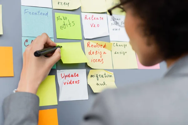 Marker in hand of african american businesswoman near board with sticky notes — Stock Photo