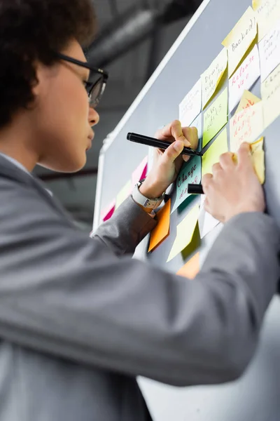 Low angle view of blurred african american businesswoman in suit writing on sticky note with marker — Stock Photo