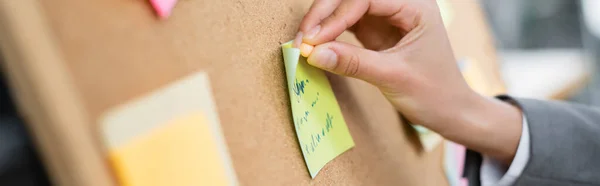 Vue recadrée de femme d'affaires attachant des notes collantes sur un tableau flou, bannière — Photo de stock