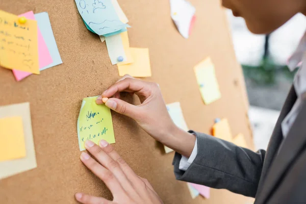 Cropped view of african american businesswoman attaching sticky note on blurred board in office — Stock Photo