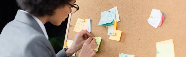 Young african american manager attaching sticky notes in office, banner — Stock Photo