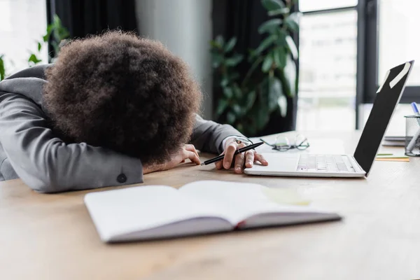 Mujer de negocios afroamericana acostada en la mesa cerca de la computadora portátil y portátil - foto de stock