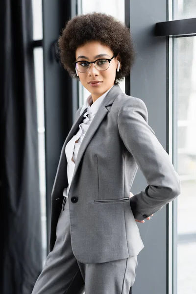 African american businesswoman in eyeglasses and earphones standing near window — Stock Photo
