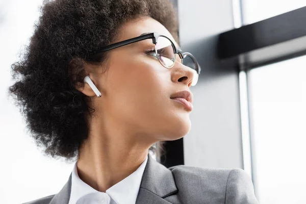 Vista de ángulo bajo de la mujer de negocios afroamericana en auriculares mirando a la ventana - foto de stock