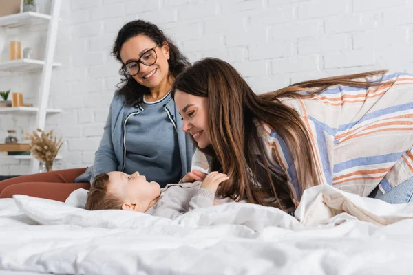 Glückliche Mutter kitzelt kleinen Jungen in der Nähe afrikanisch-amerikanischer Frau in Brille — Stockfoto