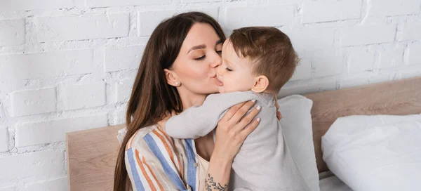 Tattooed mother kissing baby boy in romper, banner — Stock Photo