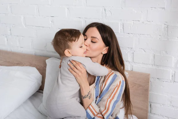 Tatoué mère baisers bébé garçon dans barboteuse — Photo de stock