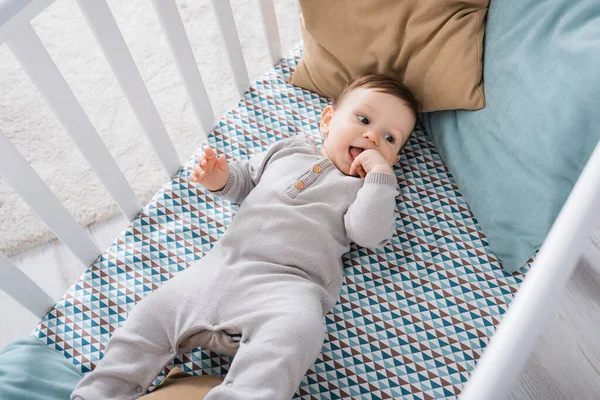 High angle view of infant boy in romper lying in baby crib — Stock Photo