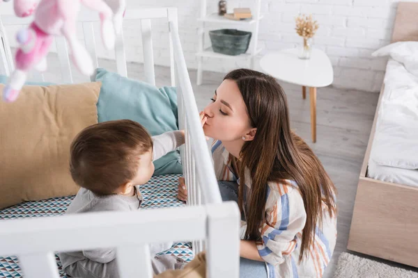 High angle view of mother kissing hand on baby boy in crib — Stock Photo