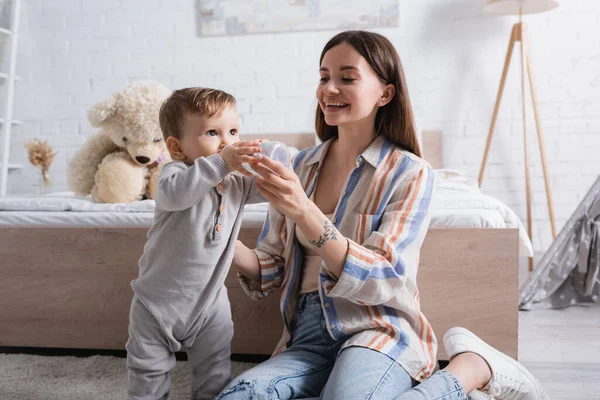 Happy tattooed mother feeding infant son with milk from bottle — Stock Photo