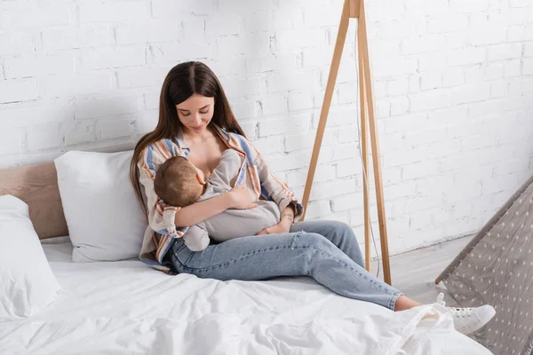Cuidado madre joven sosteniendo en brazos bebé niño en la cama - foto de stock