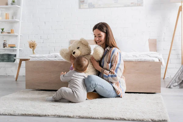 Татуйована молода мати тримає плюшевого ведмедя біля немовляти сина — стокове фото
