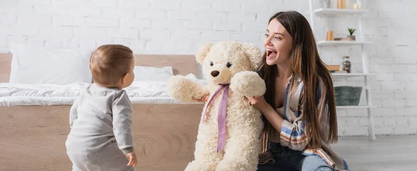 Verblüffte junge Mutter hält Teddybär in der Nähe ihres kleinen Sohnes, Transparent — Stockfoto