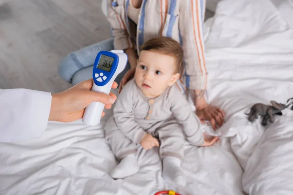 Kinderarzt untersucht Säugling mit berührungslosem Thermometer in der Nähe der Mutter — Stockfoto