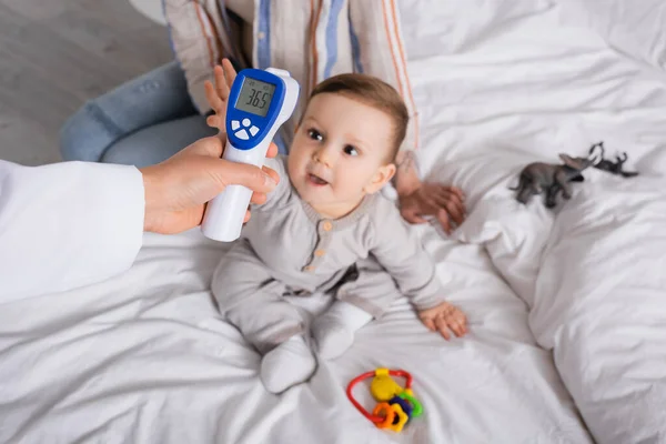 Arzt untersucht Säugling mit berührungslosem Thermometer in der Nähe der Mutter — Stockfoto