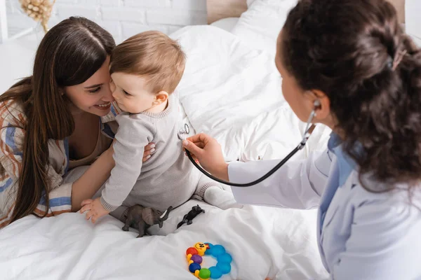 Pédiatre afro-américain en manteau blanc examinant un bébé garçon avec stéthoscope — Photo de stock