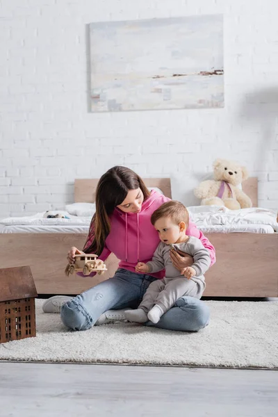 Joven madre y niño jugando con coche de madera cerca de la casa de juguete - foto de stock