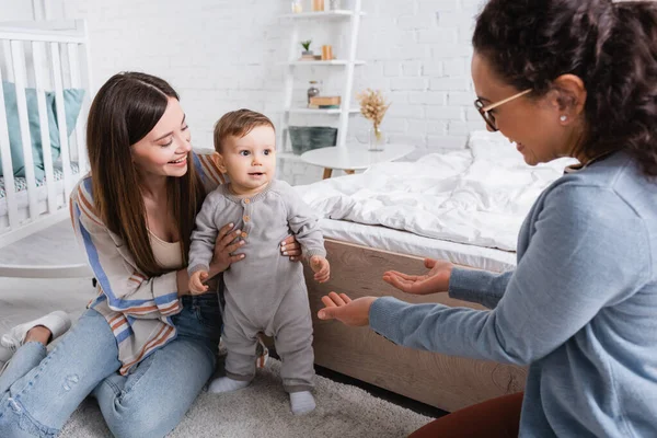 Verschwommene afrikanisch-amerikanische Frau mit ausgestreckten Händen in der Nähe von Säugling mit Mutter — Stockfoto