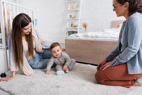 Женщины смотрят на младенца, сидящего на ковре — стоковое фото