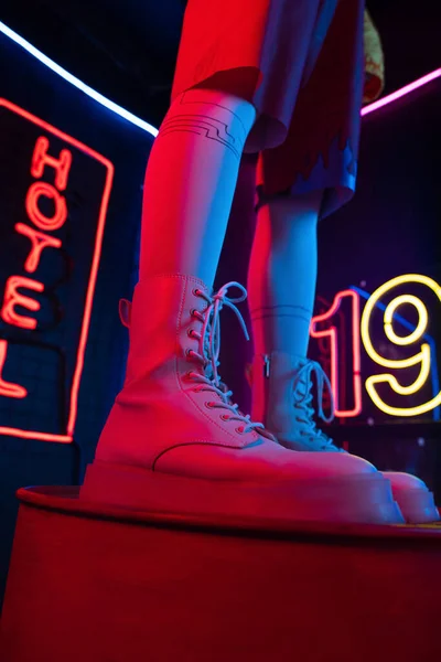 Cropped view of young woman in trendy white sneakers standing near neon sign with hotel lettering — Stock Photo