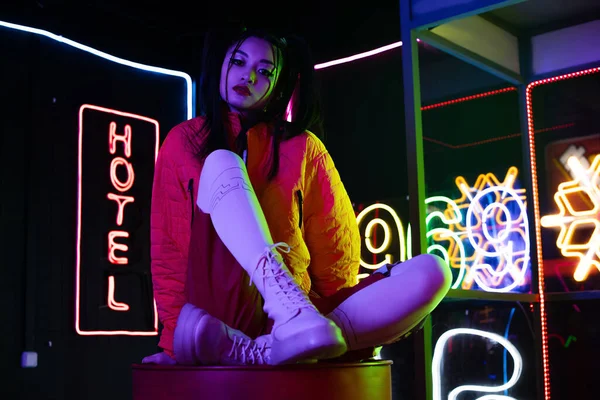 Young asian woman sitting near neon sign with hotel lettering outside - foto de stock