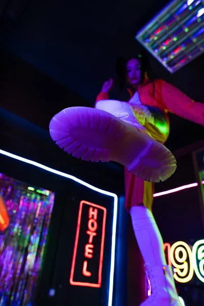 Low angle view of blurred young asian woman in white shoes near neon sign with hotel lettering outside — Photo de stock