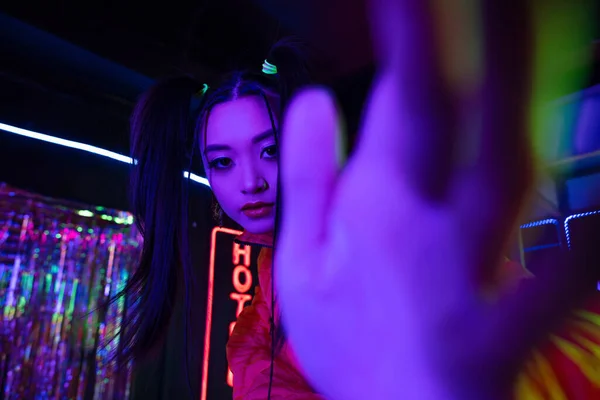 Young asian woman with blurred hand near neon sign with hotel lettering outside — Fotografia de Stock