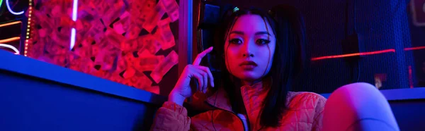 Young asian woman looking away near neon lighting, banner — Foto stock