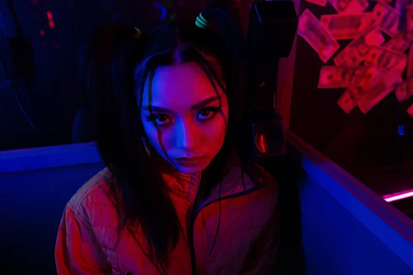 Stylish young asian woman looking at camera near neon lighting — Photo de stock