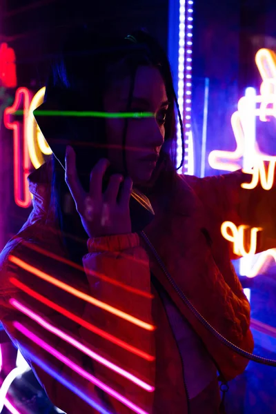 Neon lighting on young asian woman talking on retro payphone outside — Photo de stock