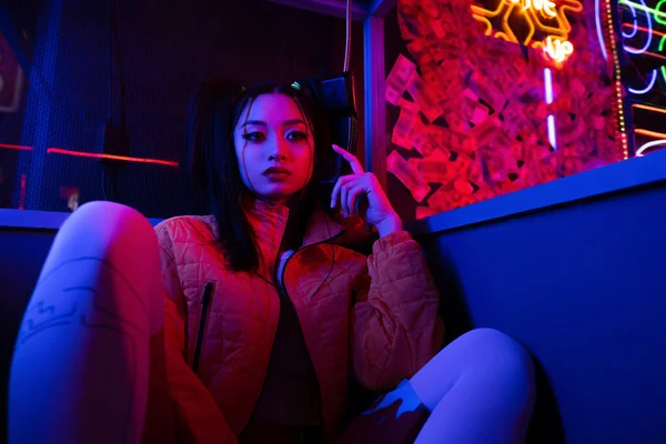 Неоновое освещение на стильную молодую азиатскую женщину, разговаривающую по ретро-телефону снаружи — стоковое фото