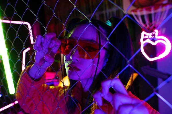 Trendy young asian woman in sunglasses looking at camera through metallic fence — Stock Photo