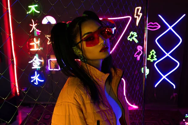 Young asian woman in sunglasses looking at camera near neon sign - foto de stock