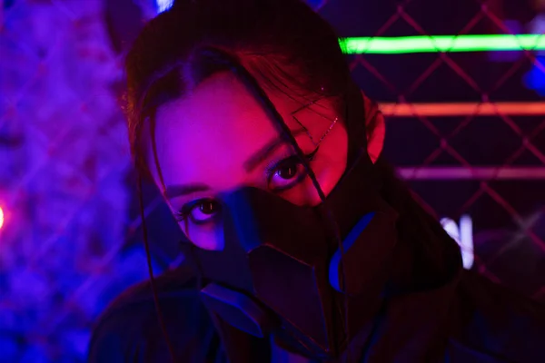 Neon lighting on young asian woman in gas mask looking at camera — Fotografia de Stock