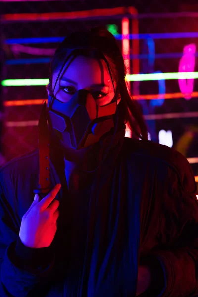 Neon lighting on young asian woman in gas mask holding knife - foto de stock