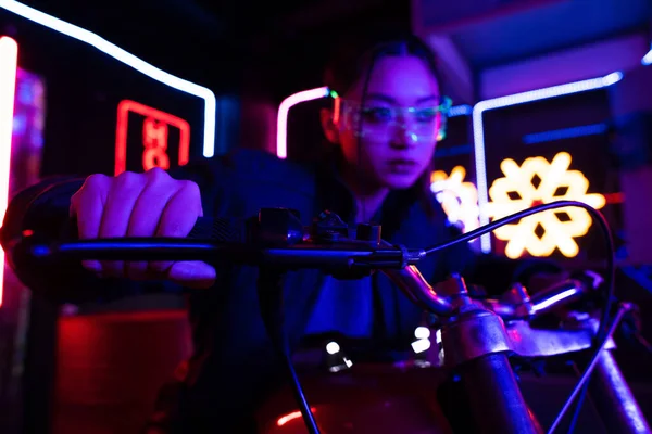 Blurred young asian woman in sunglasses riding motorcycle near neon sign outside — Fotografia de Stock