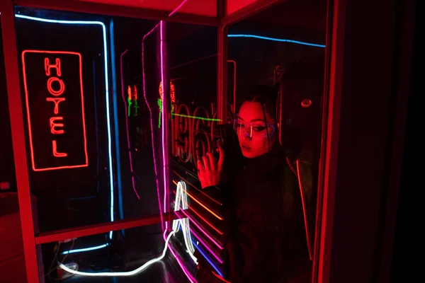 Armed asian woman in sunglasses holding gun near neon hotel sign — Foto stock
