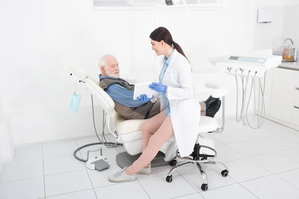 Dentiste souriant montrant comprimé au patient âgé en clinique dentaire — Photo de stock