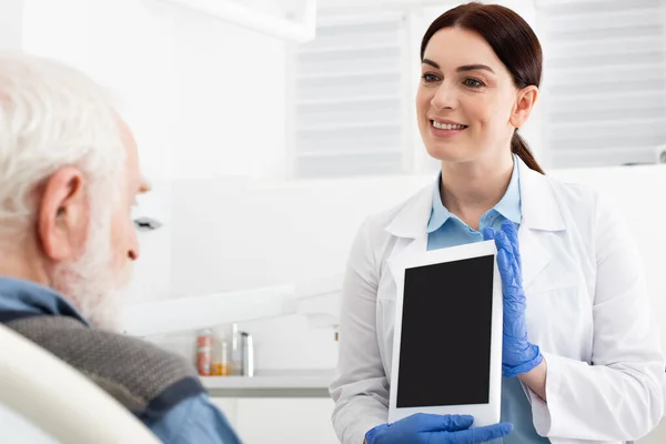 Dentista alegre mostrando tableta a paciente mayor en clínica dental - foto de stock