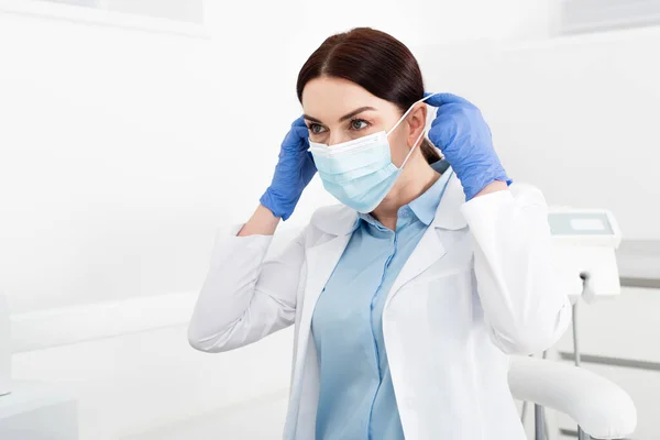 Dentista em luvas de látex usando máscara médica na clínica odontológica — Fotografia de Stock
