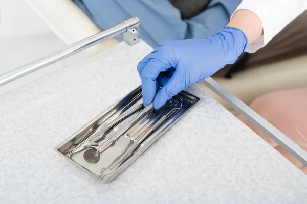 Vista cortada do dentista em luva de látex tendo espelho de bandeja de metal na mesa na clínica odontológica — Fotografia de Stock