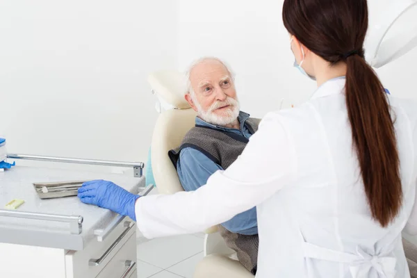 Sorridente idoso recebendo consulta de dentista em luvas de látex na clínica odontológica — Fotografia de Stock