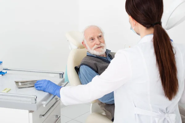 Sonriente hombre mayor recibiendo consulta de dentista en guantes de látex en clínica dental - foto de stock