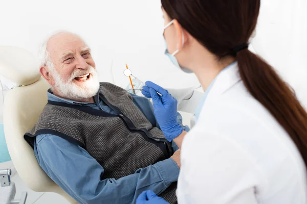Homme âgé souriant ayant des soins dentaires par le dentiste dans des gants en latex dans une clinique dentaire — Photo de stock
