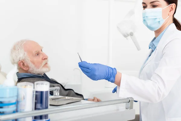 Старший человек, проходящий лечение зубов стоматологом в латексных перчатках в стоматологической клинике — стоковое фото