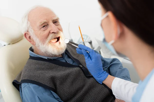 Hombre mayor que tiene examen de dientes por dentista en guantes de látex con espejo en silla dental - foto de stock