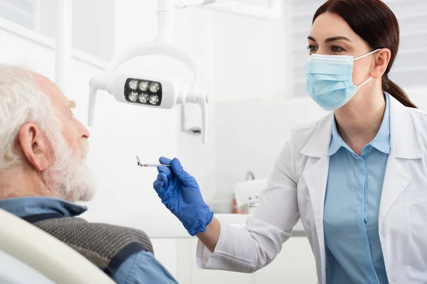 Hombre mayor que tiene examen de dientes por dentista en guantes de látex con espejo en silla dental - foto de stock