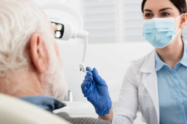 Senior ayant un examen dentaire par un dentiste en gants de latex avec miroir à la clinique — Photo de stock
