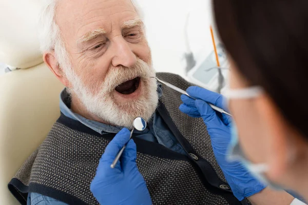 Homem idoso tendo exame dentário por dentista em luvas de látex com sonda e espelho na clínica — Fotografia de Stock