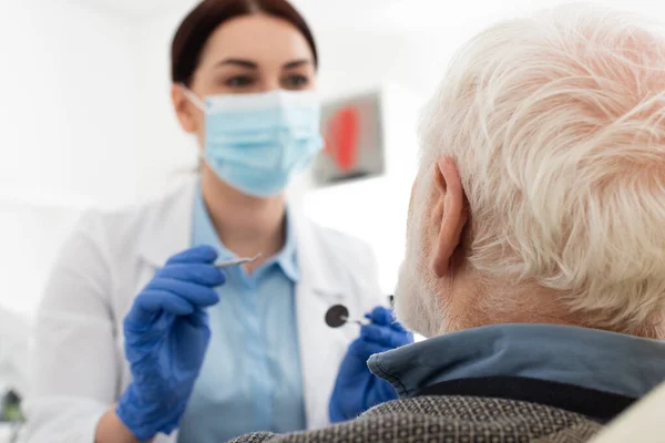 Dentist in medical mask examining teeth of senior man with probe and mirror in dental chair — Stock Photo